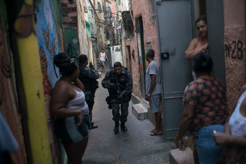 “A police officer patrols among residents during an operation against drug traffickers at the ‘pacified’ Jacarezinho slum in Rio de Janeiro, Brazil.”